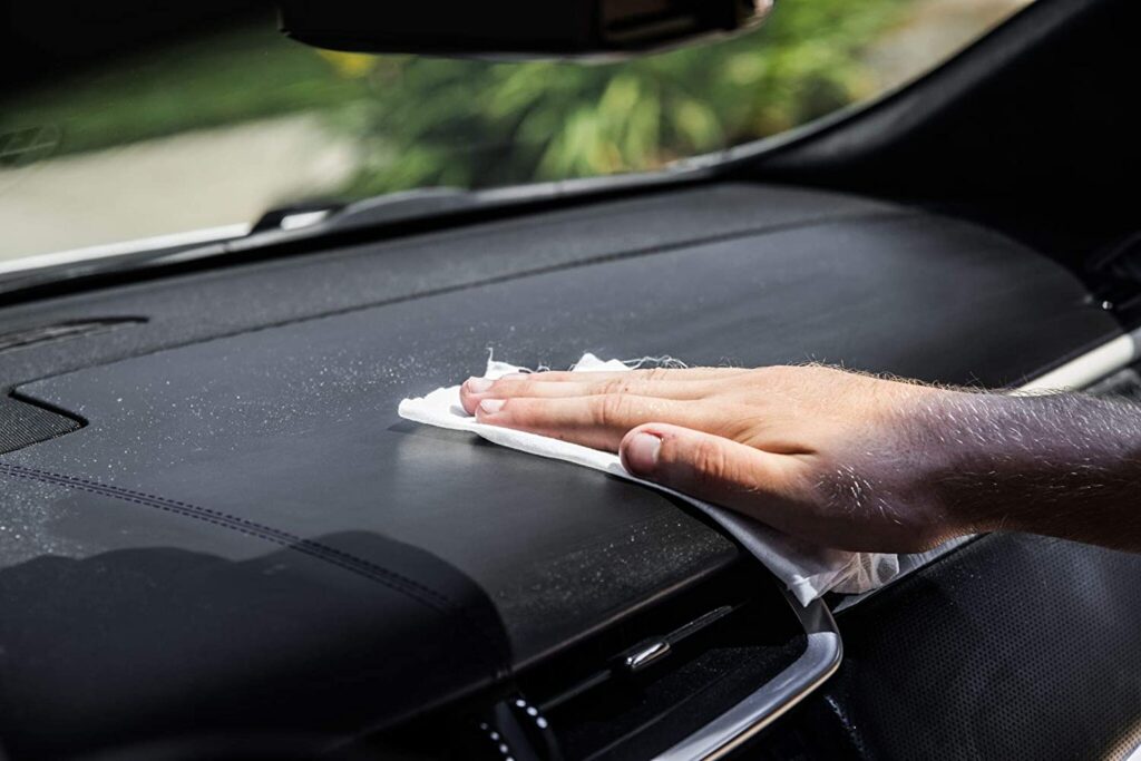 a person cleaning the dashboard of a car using a disinfection wipe
