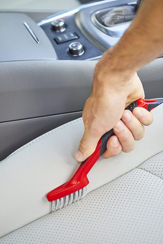 a person cleaning the car’s seat with a red brush