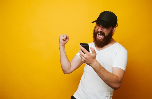 Happy bearded man celebrate success and looking at phone