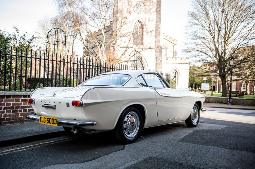 A white Volvo P1800 parked on the side of a street during daytime.