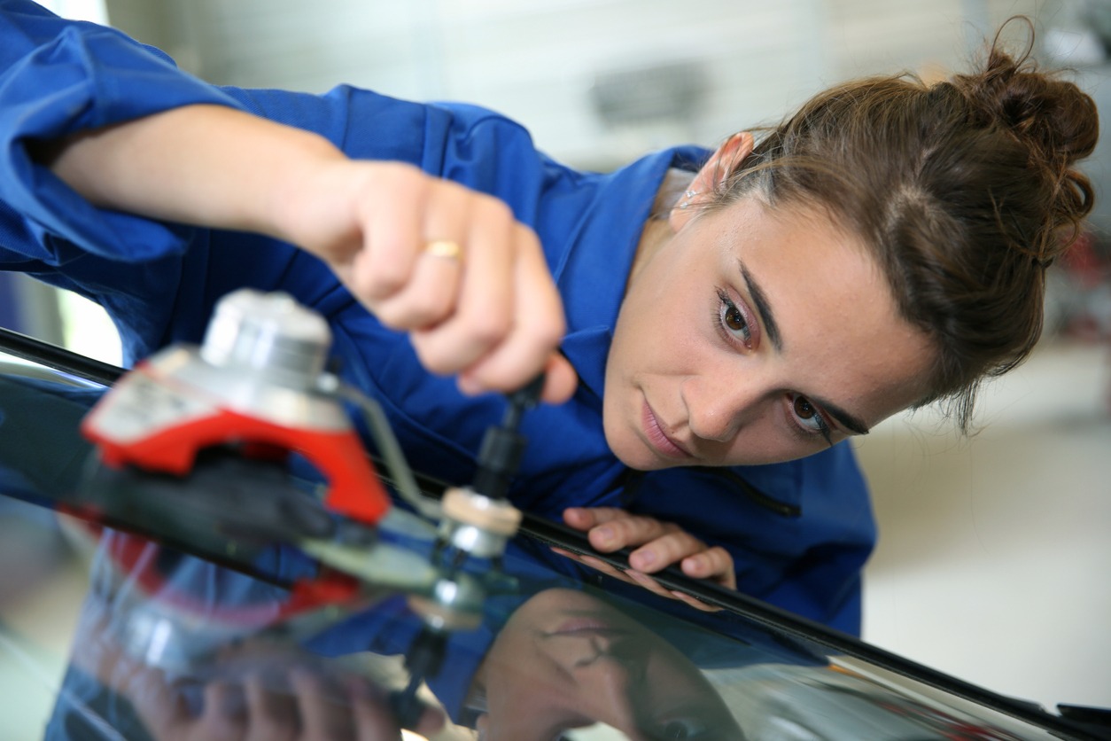 Student changing car windshield in auto shop