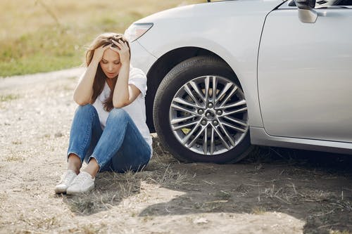 Worried woman sitting near broken car at the roadside
