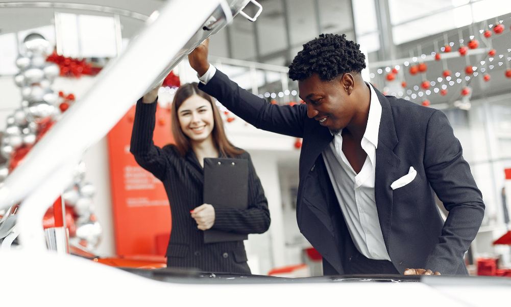 happy-man-checking-under-car-hood-in-car-showroom