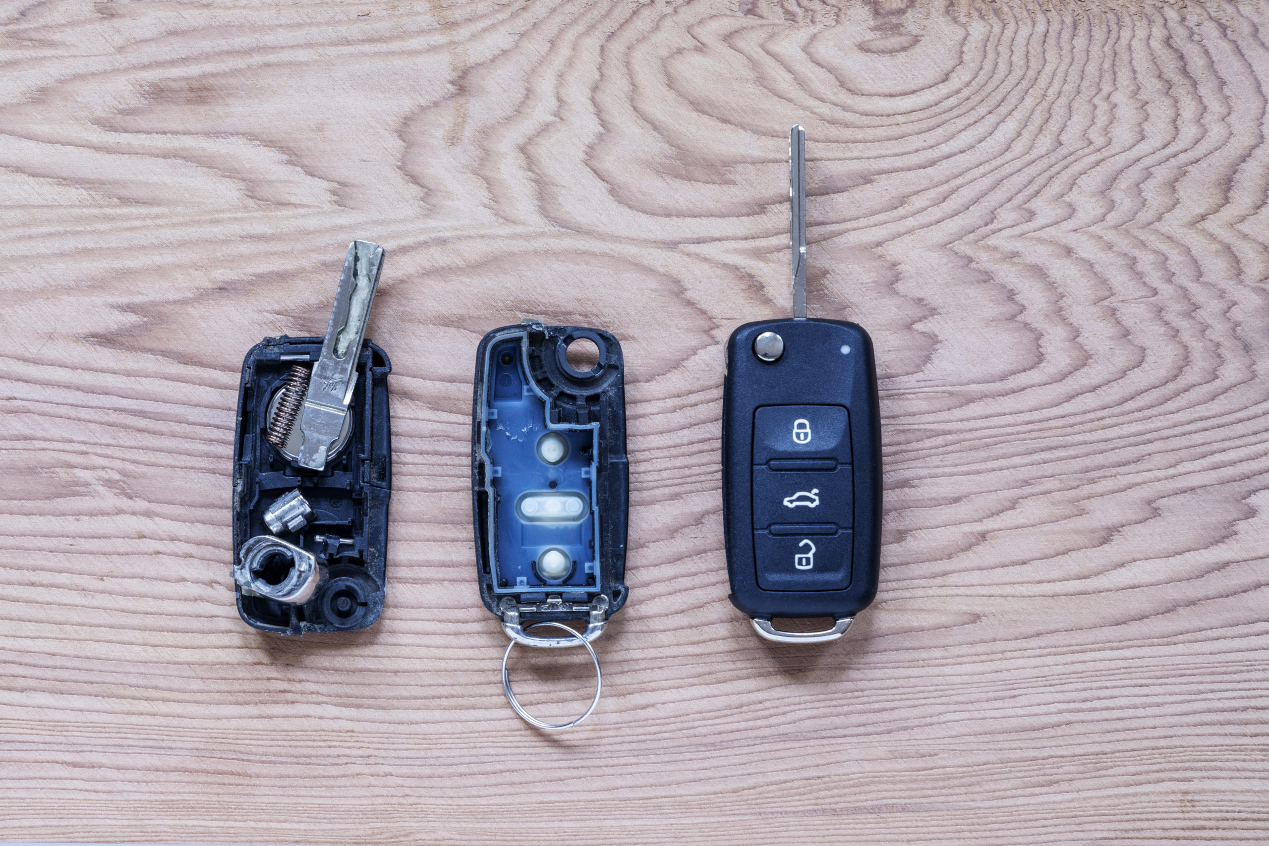 Broken or damaged remote key fob and new vehicle key on wooden b