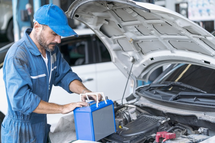 a car mechanic is replacing the battery of a car with a car batter carrier