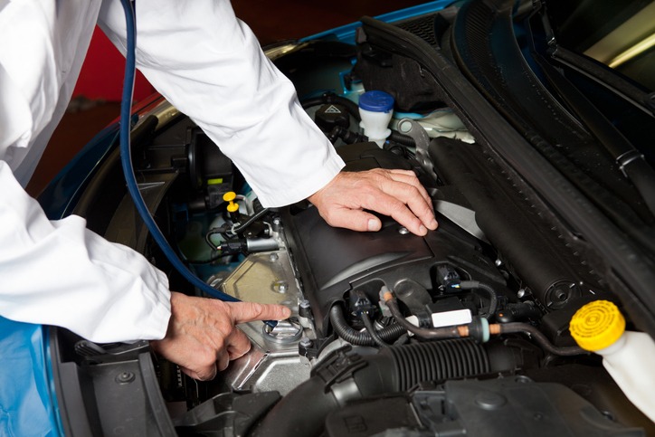 a car mechanic wearing a white overall and checking the car engine with a stethoscope