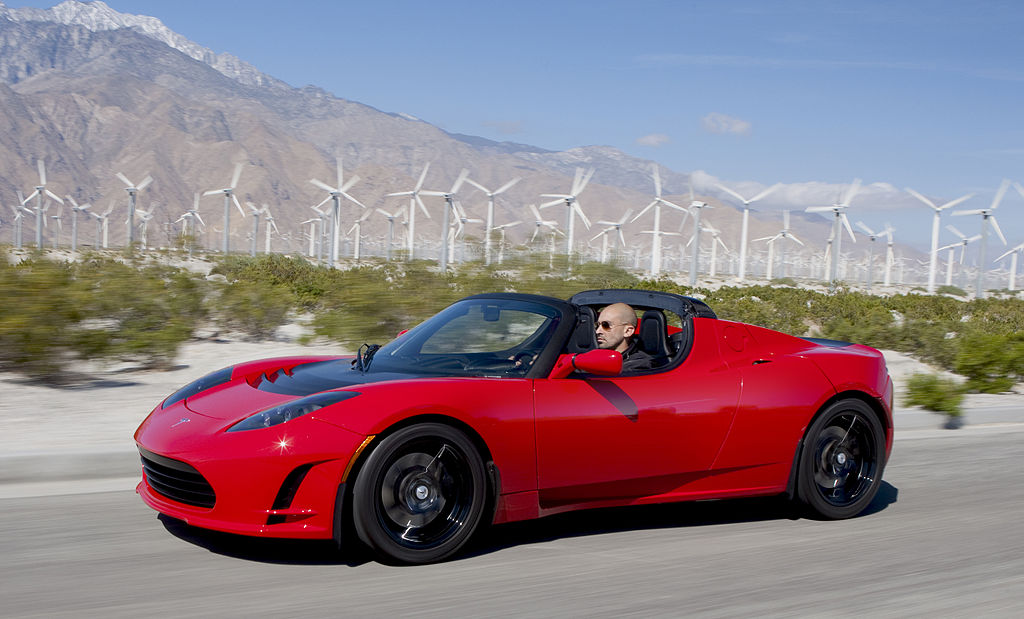 a man driving the Tesla Roadster Sport 2.5, plants, windmills, and a mountain at the background