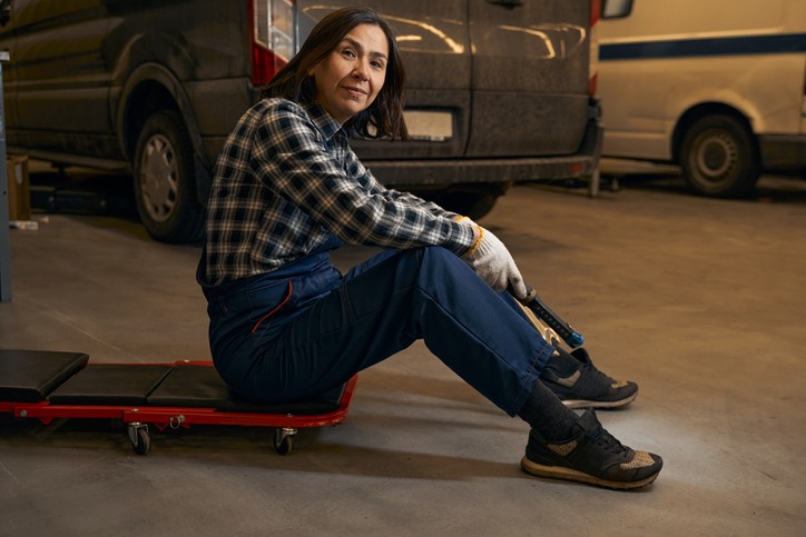 a woman sitting on a regular padded creeper and holding a wrench