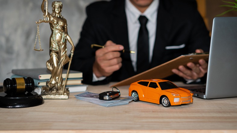 Small cars, keys and scales. Goddess of justice with hammer, money and laptop, and businessman holding a pen to sign a contract under car title approval concept.