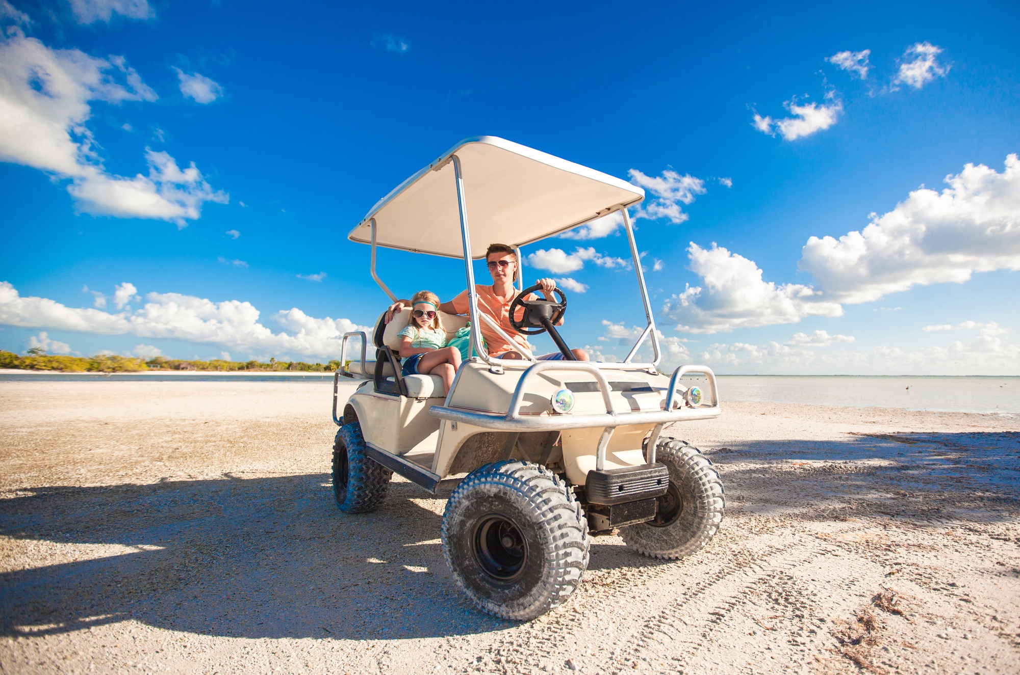 Dad with his two daughters driving golf cart at tropical beach