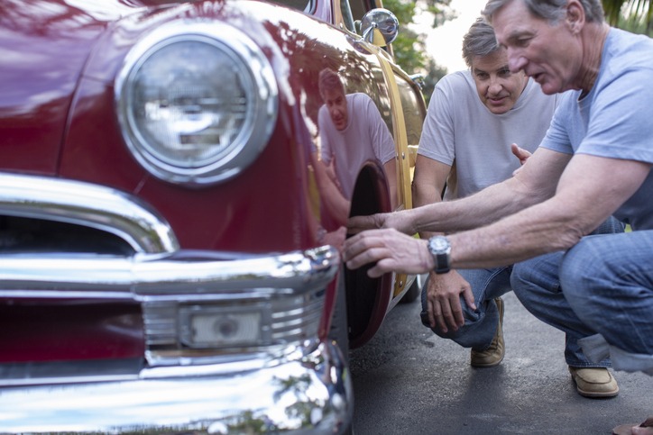 Male friends inspecting tire on vintage woody wagon