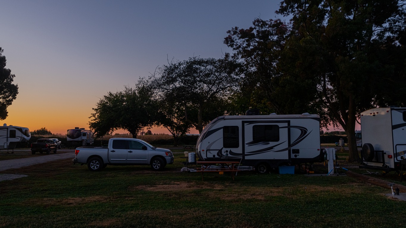a-vehicle-and-a-small-trailer-parked-in-a-grassy-campsite-at-dawn