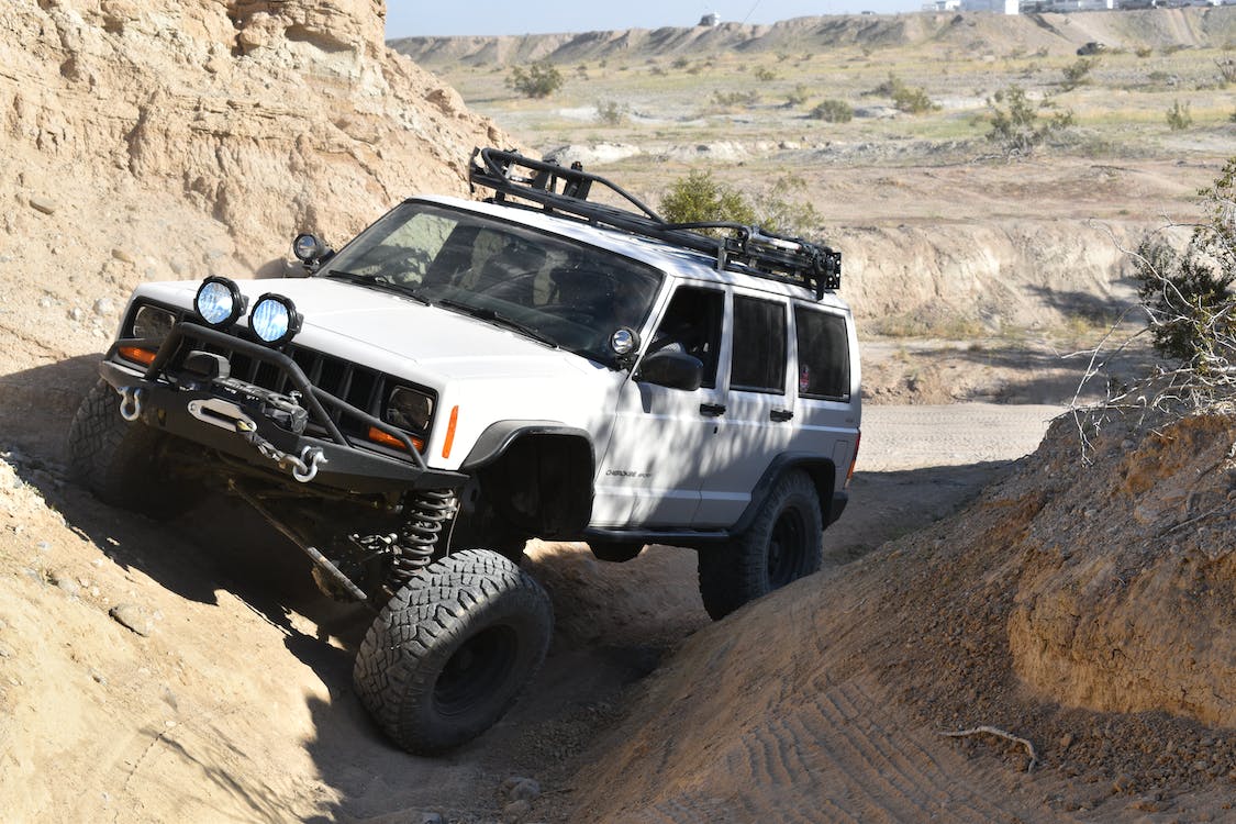 white jeep with suspension lift kit driving through rugged rocky terrain