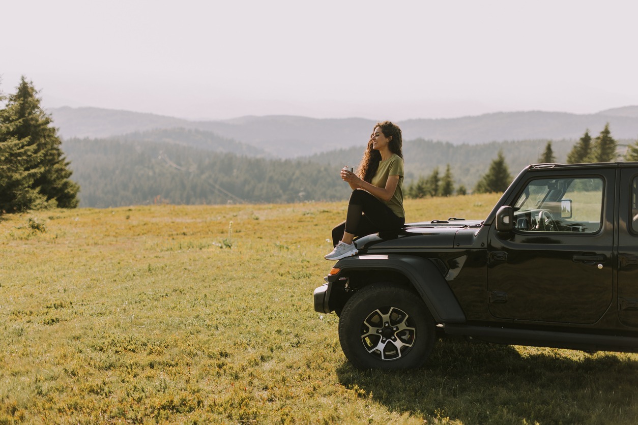 woman feeling happy and relaxed while sitting on a car and admiring nature